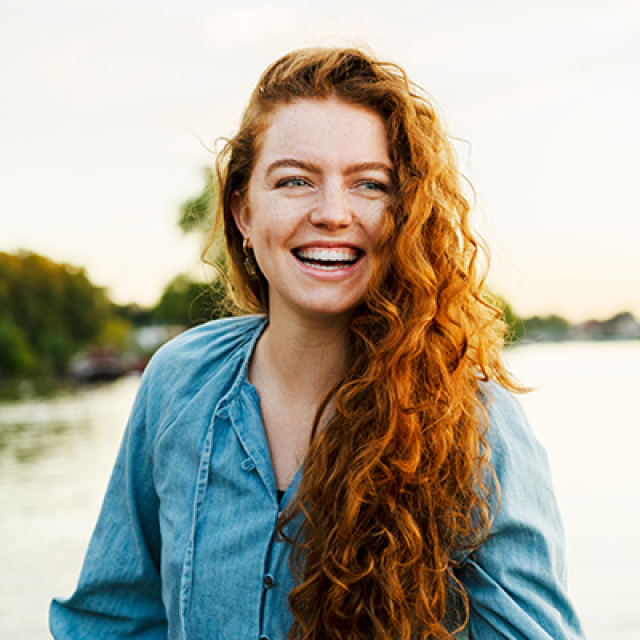 Young woman with curly red hair smiles while standing near water