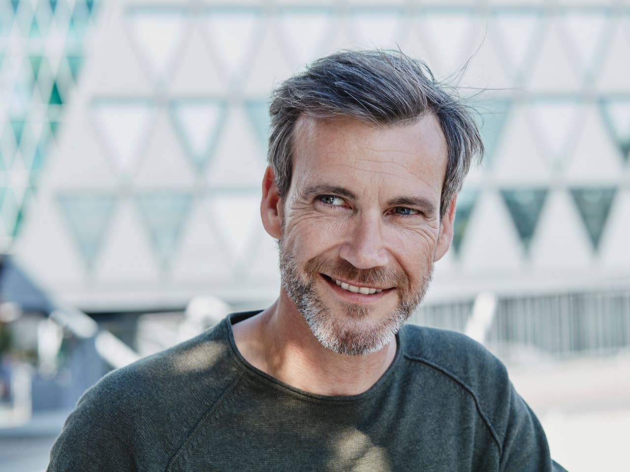 Smiling middle-aged white man with brown/grey hair and a beard stands outdoors in the sunshine