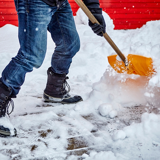 A person shoveling snow from a driveway, wearing winter clothing.