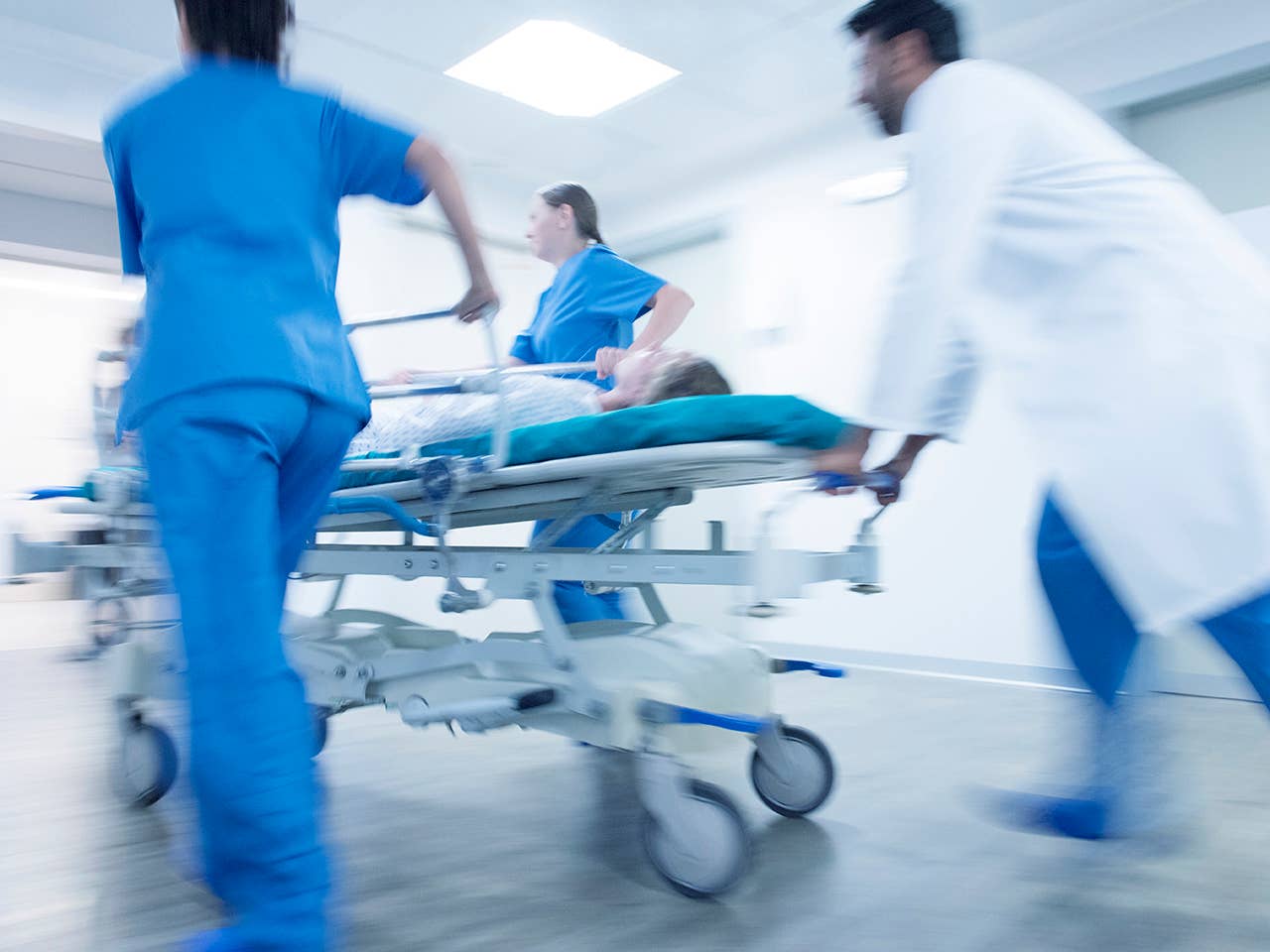 Doctor in a white lab coat and two nurses in light blue scrubs push a hospital gurney down a hallway
