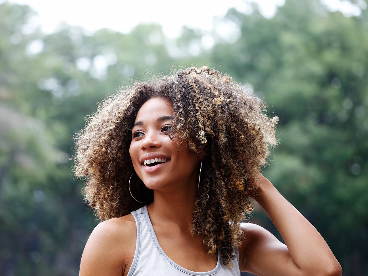 Smiling Black woman with curly hair standing outside near trees