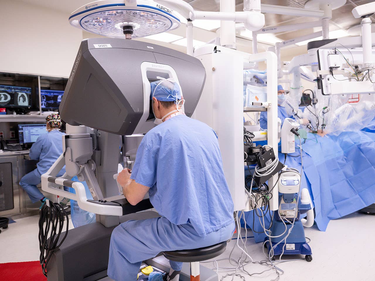 Surgeon in light blue scrubs sits at robotic surgery equipment in the operating room