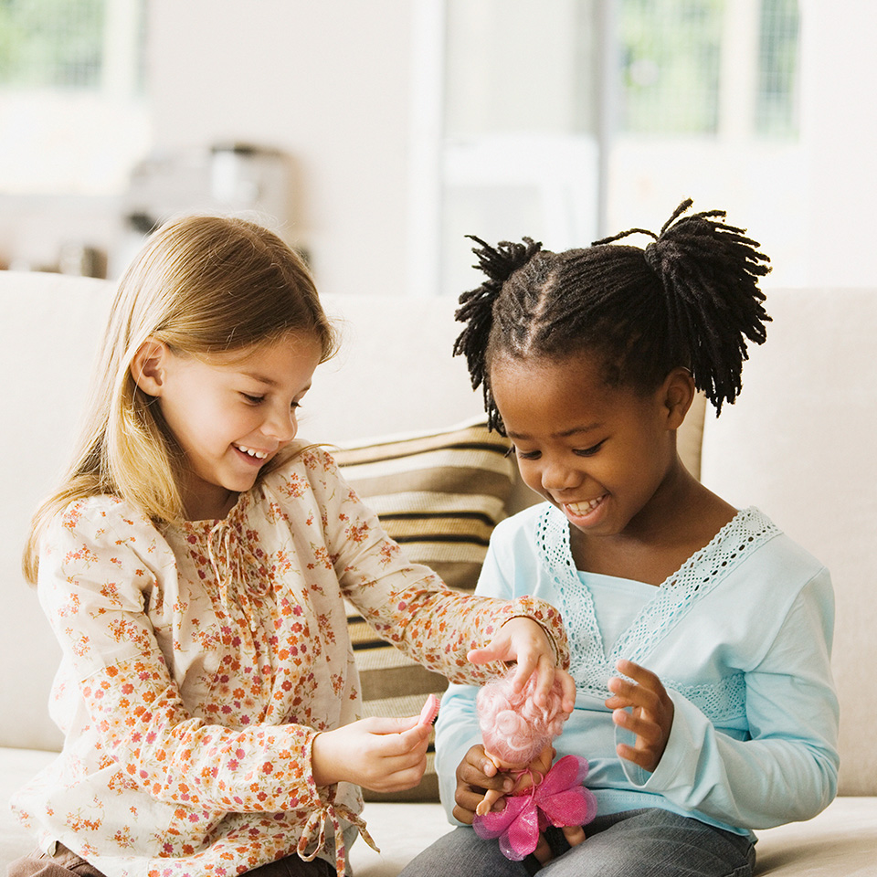 Smiling white girl hands a doll to a smiling African American girl