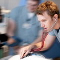A man in scrubs attentively examines a patient, showcasing the dedication of our residents in healthcare.