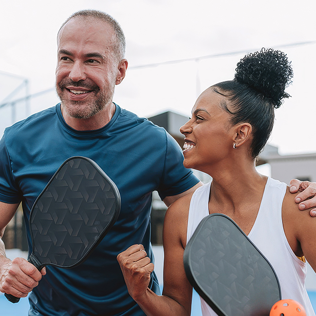 Two people holding pickleball paddles on an outdoor court, highlighting an active lifestyle supported by healthy nutrition.