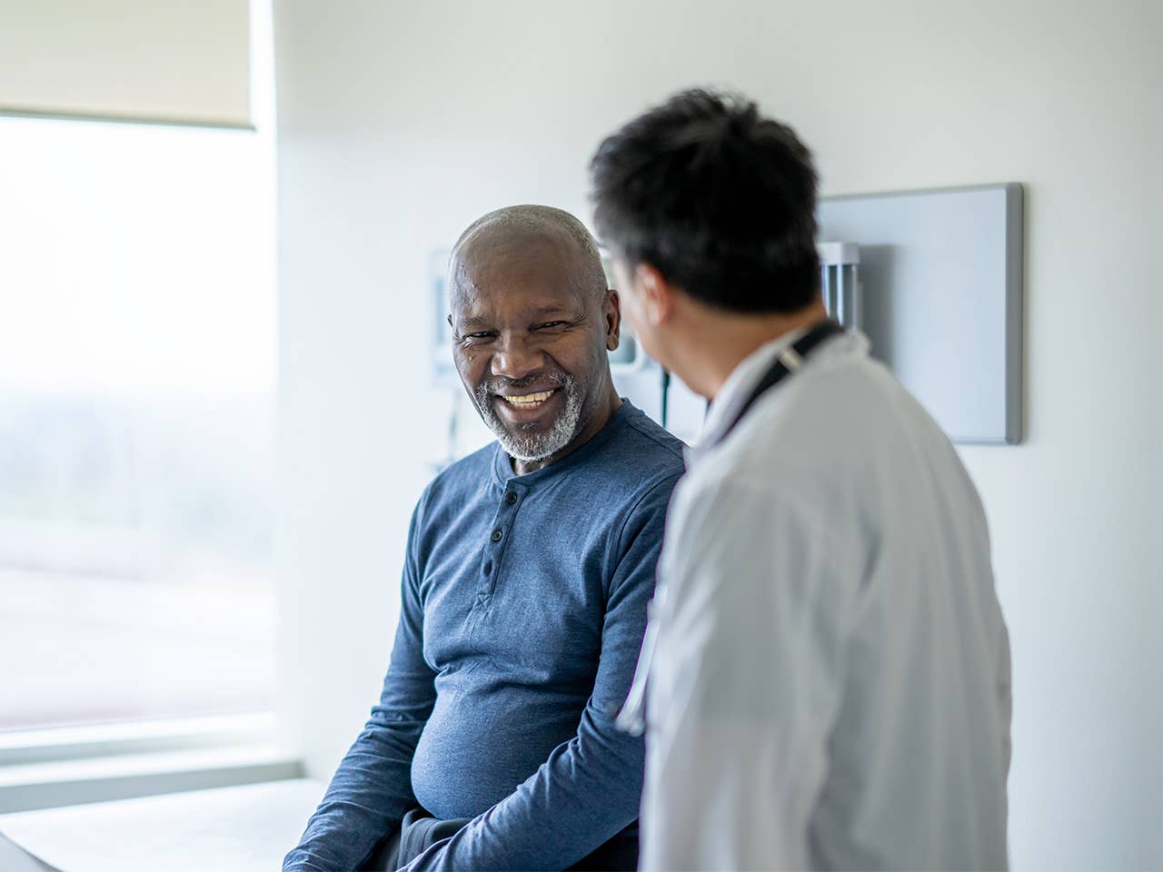 Smiling middle aged Black man speaks with a Corewell Health ear, nose, and throat surgeon in an exam room