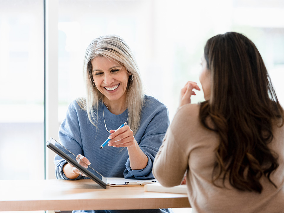 Smiling speech therapist points at the screen of a tablet while speaking with a female patient