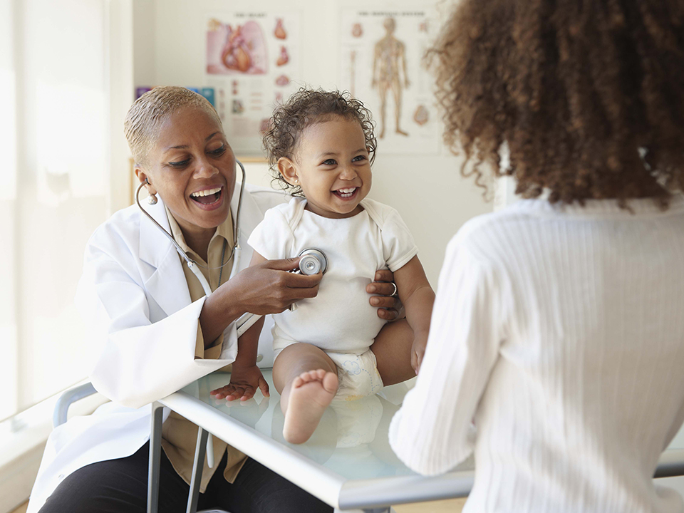 A woman smiles at a doctor while cradling her baby in her arms.