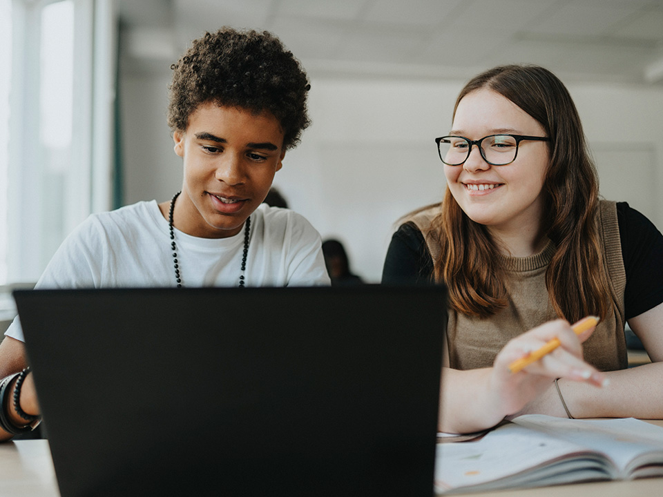 Two smiling students look at a laptop, engaged in a collaborative learning experience.