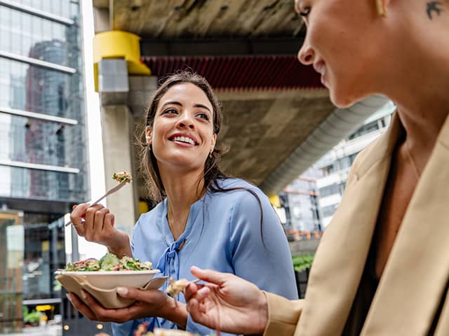 Two people eating fresh salad bowls outdoors in an urban setting, making healthy meal choices on the go.