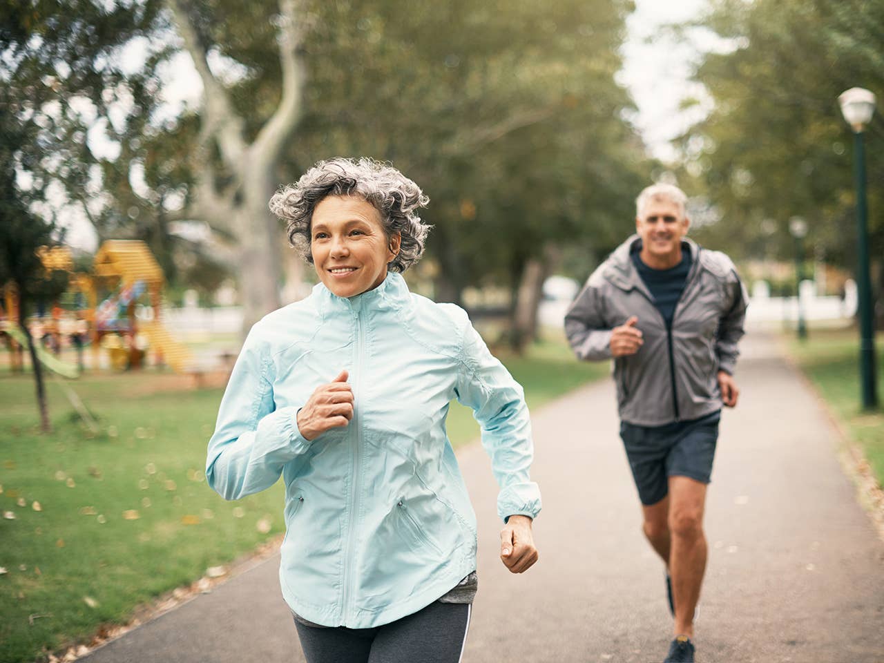 Older man and woman jog together in a park