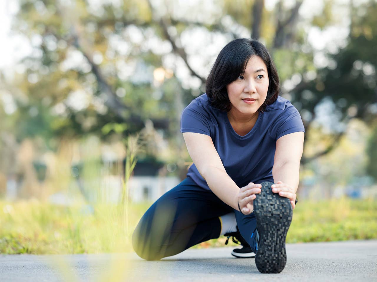 Young Asian woman stretches her leg outdoors in the sunshine before jogging