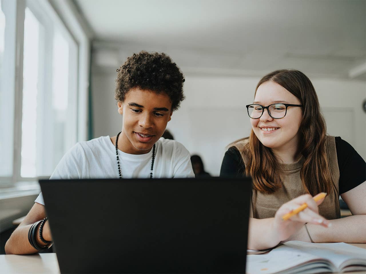Two young individuals are focused on a laptop screen, engaged in a discussion or activity together.