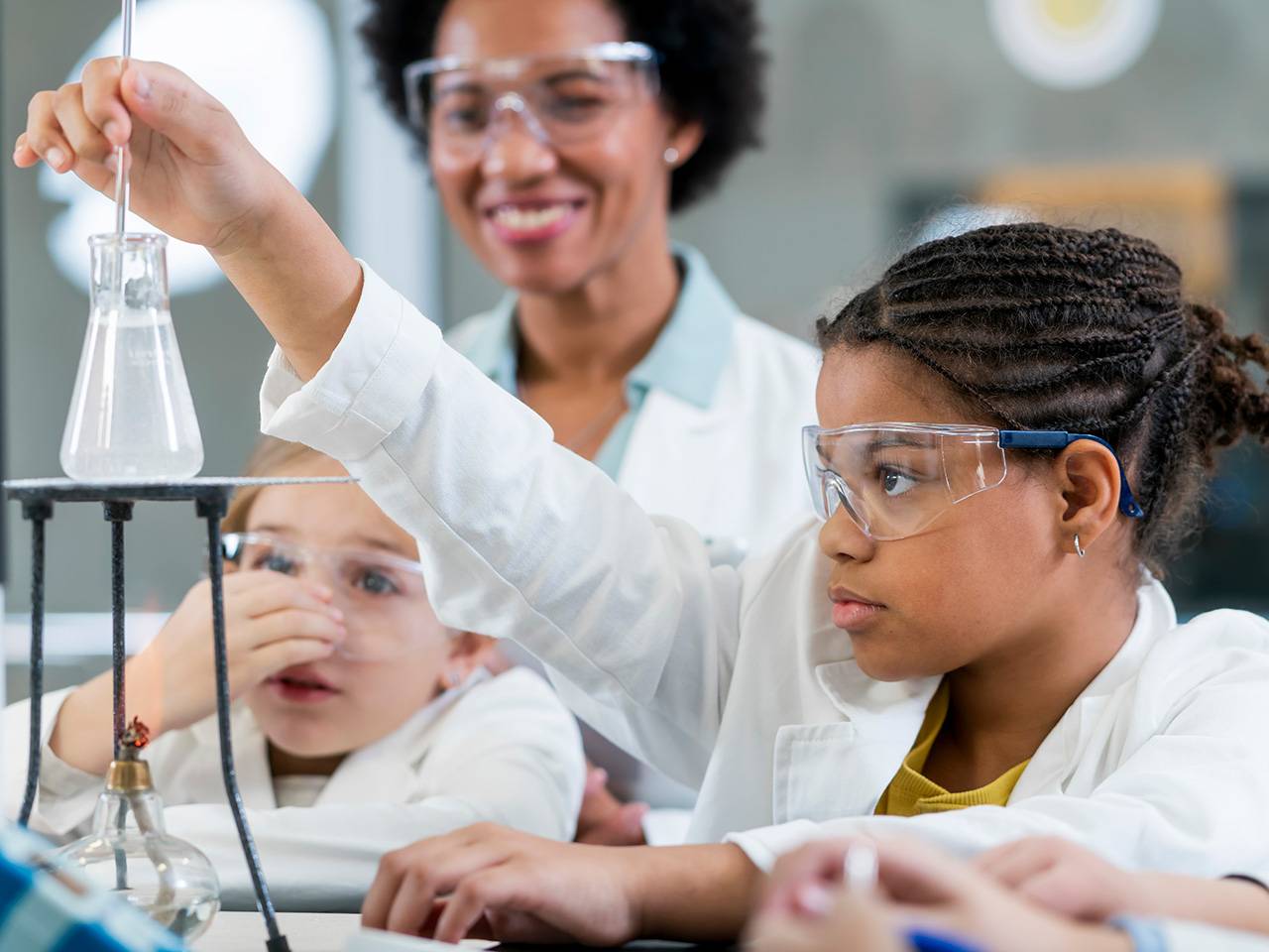 A group of children wearing lab coats and glasses, engaged in a science activity together.