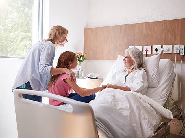 Mother and daughter visiting an elderly woman in her hospital bed at the hospital