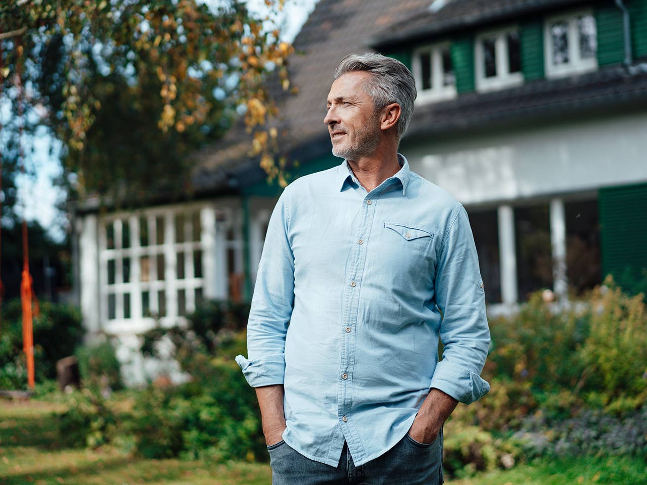 Older white man stands in front of a house in the afternoon