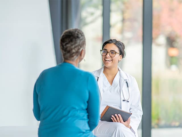 A female doctor is smiling and having a conversation with her female patient with holding a tablet