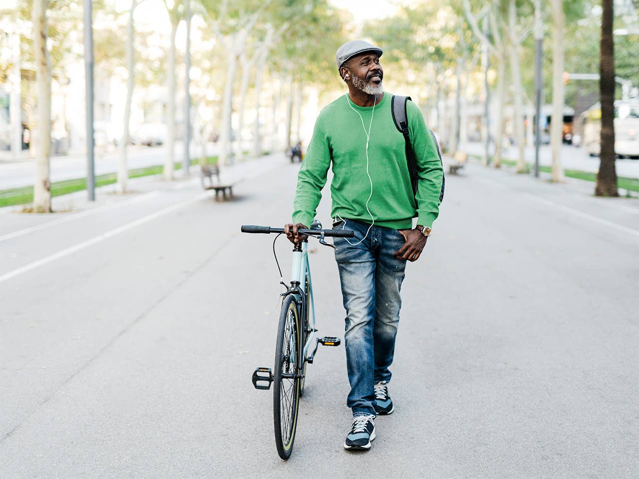 Middle aged Black man wearing a green sweater walks his bike through a park