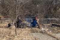 A diverse group of individuals seated by a roadside, engaged in conversation near a fence, highlighting community connection.