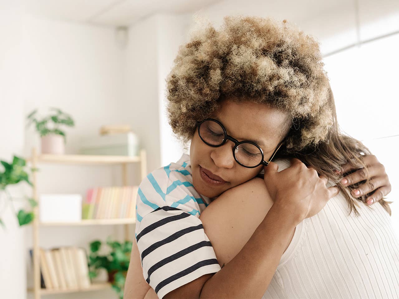 A woman wearing glasses embraces another woman, both smiling warmly in a moment of friendship and affection.