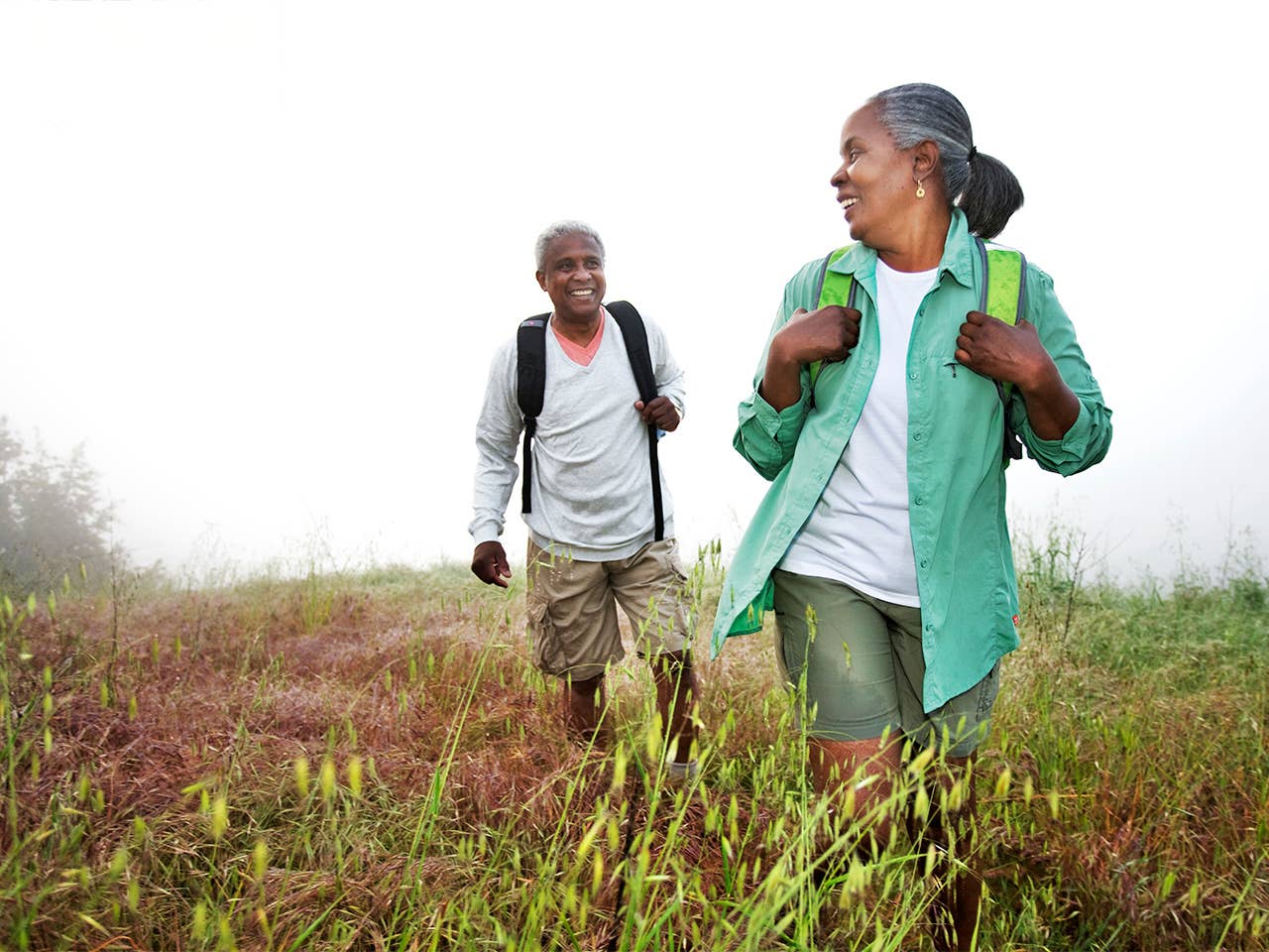 Older Black man and woman hike together through a field