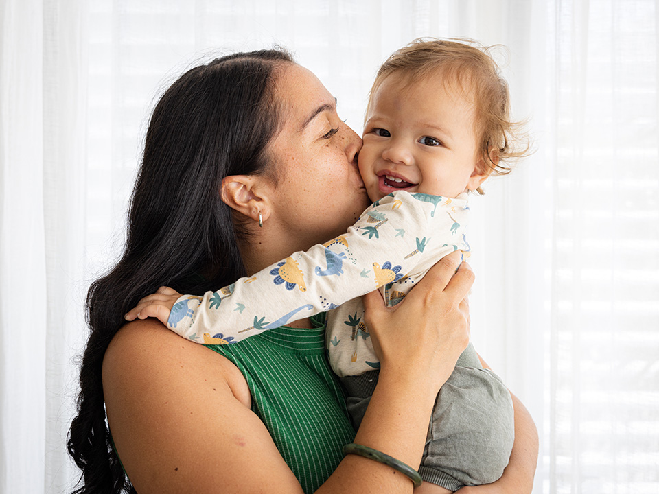Happy mother with long black hair holds and kisses her smiling baby