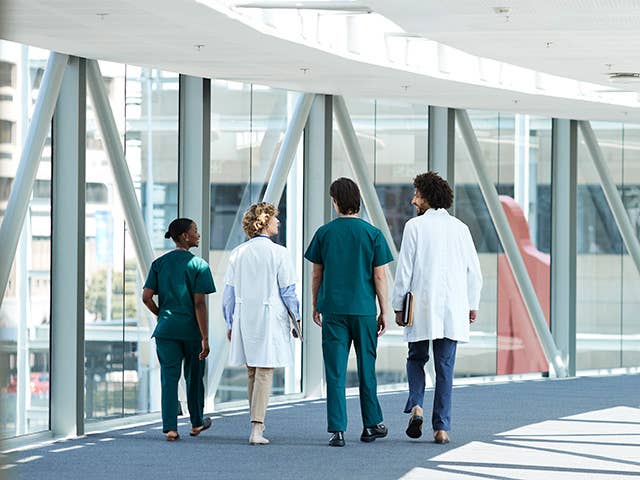 Three doctors walking together in a hallway, representing teamwork in clinical research and the pursuit of healing.