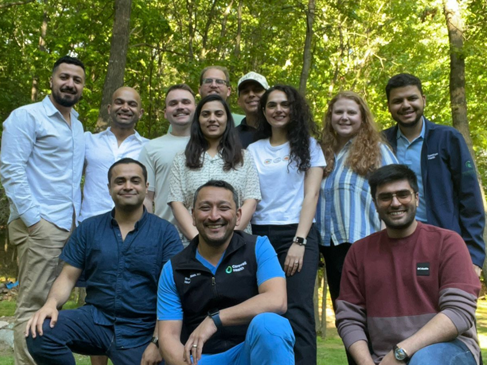 A group of people standing together outdoors in a wooded area on a sunny day, posing for a group photo.
