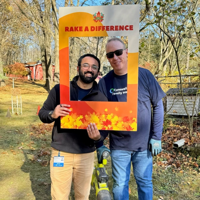 Resident and team member posing for a photo in a photo frame outside while raking for a community outreach project