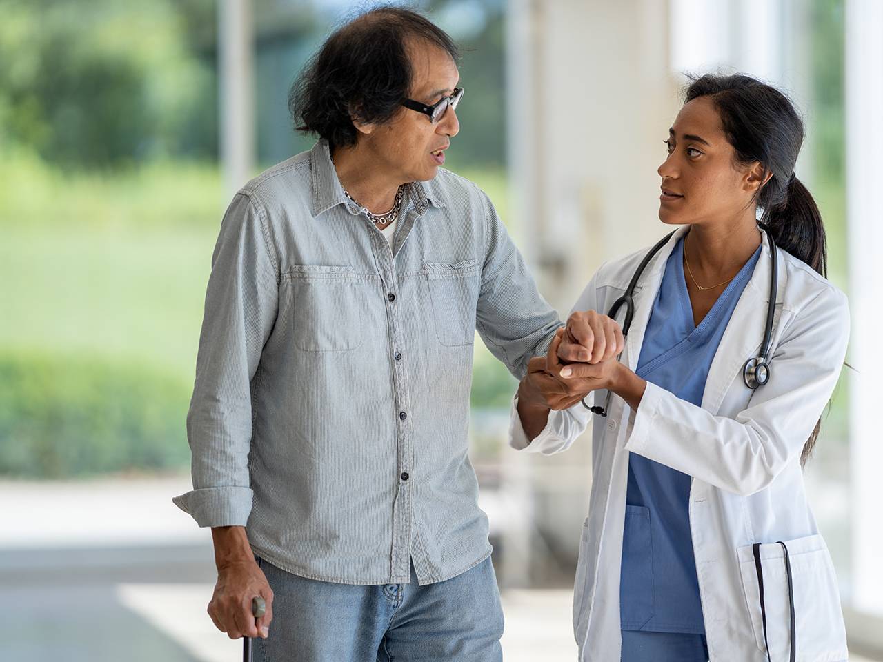 A doctor and patient stroll through a hospital corridor, engaged in conversation about medical care.