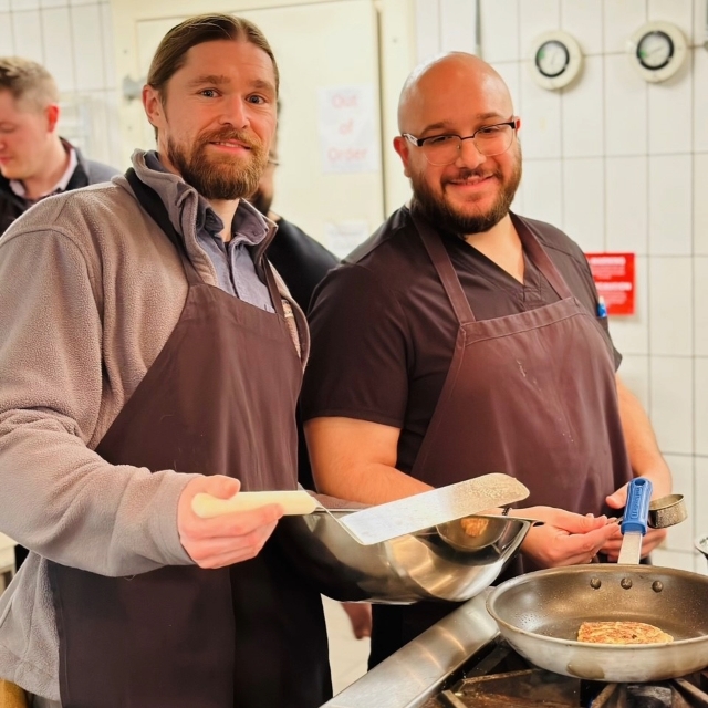 Two male chefs smiling while in the kitchen preparing food