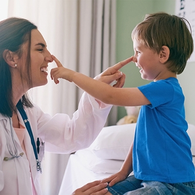 Young boy in blue shirt reaches out to touch nose of female doctor