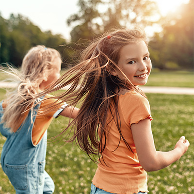 Young girl in orange t-shirt smiles at camera while running in the grass