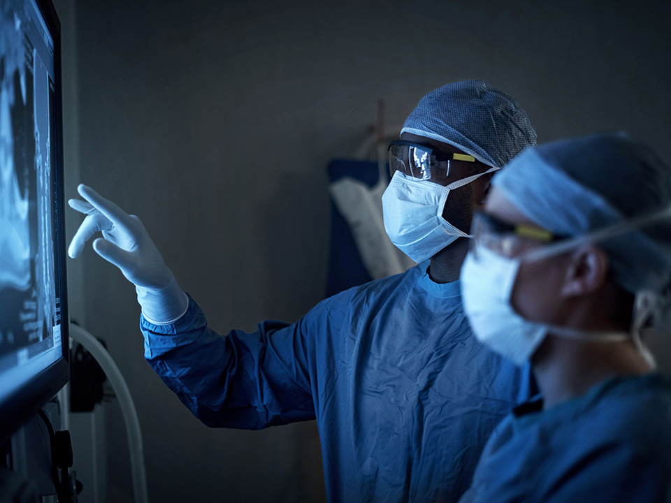 Corewell Health ear, nose, and throat surgeon points at patient imaging while in the operating room