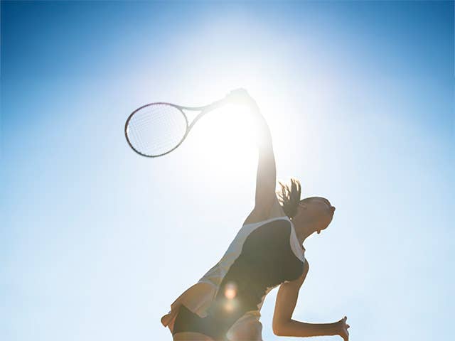 Woman swings a tennis racket in the bright sunshine