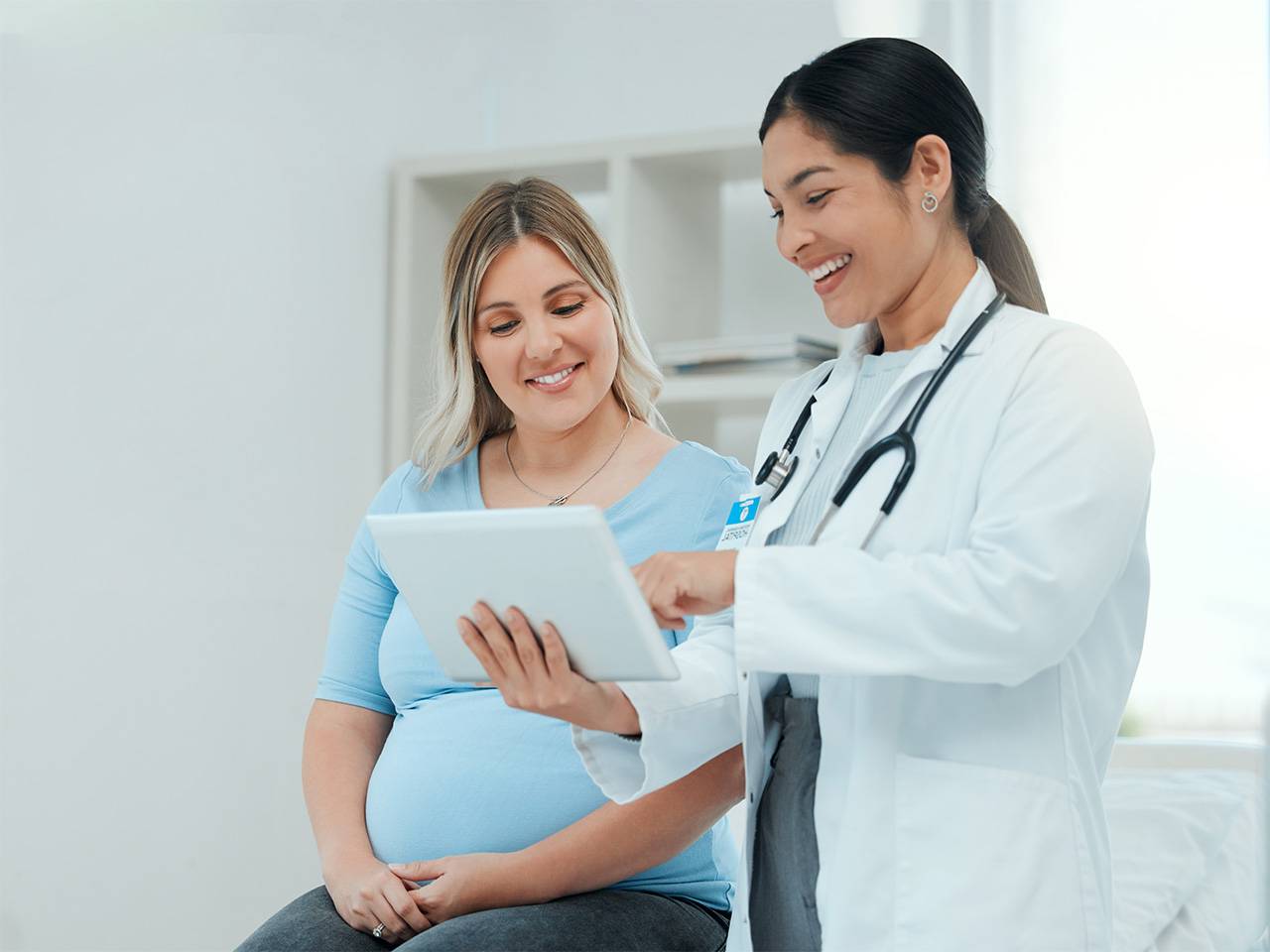 A female doctor is talking to a showing a pregnant female patient something on a tablet