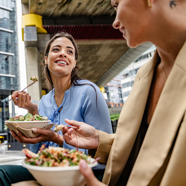 Two people eating fresh salad bowls outdoors in an urban setting, making healthy meal choices on the go.