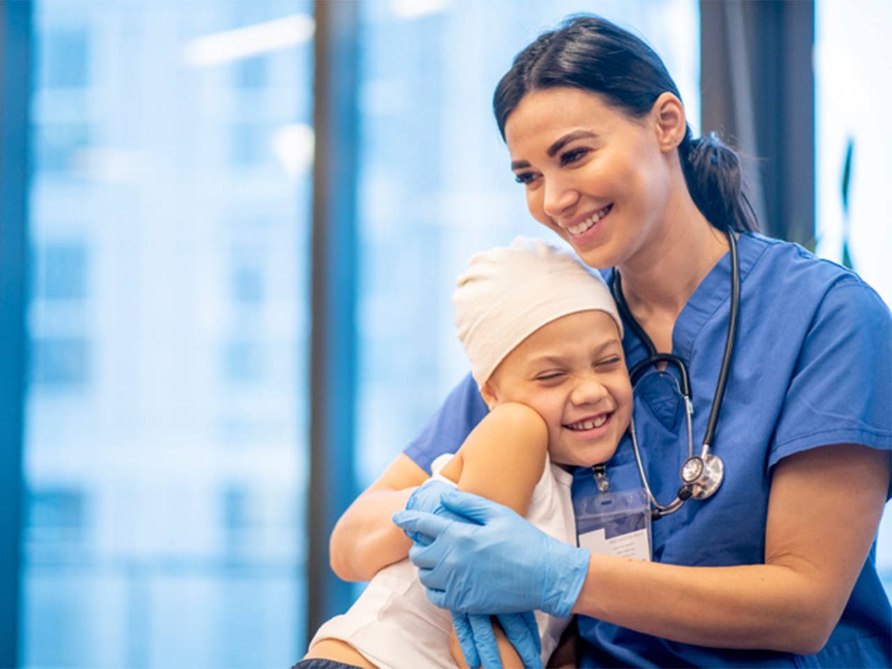 Woman in blue scrubs puts arms around smiling child