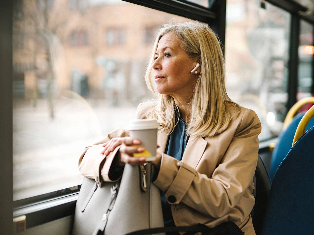 Middle aged white woman sits on a bus while wearing earbuds