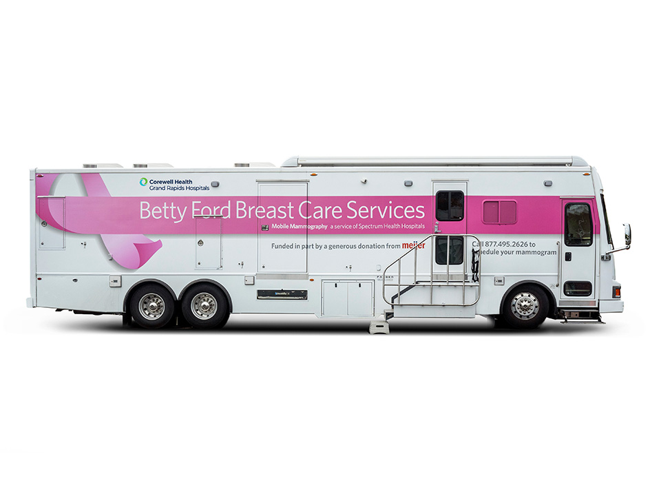 The Corewell Health mobile mammography bus, a white bus with a pink stripe and pink breast cancer ribbon on the side
