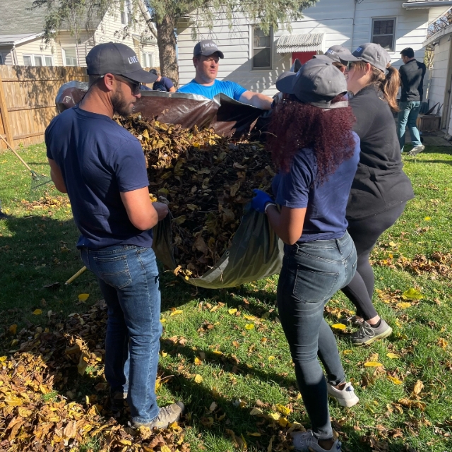 Group of people lifting a tarp full of leaves
