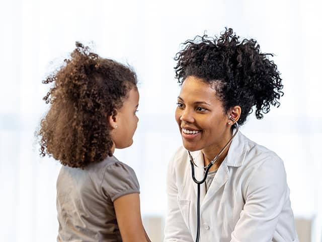 Healthcare provider using a stethoscope to examine a young child during a pediatric visit.