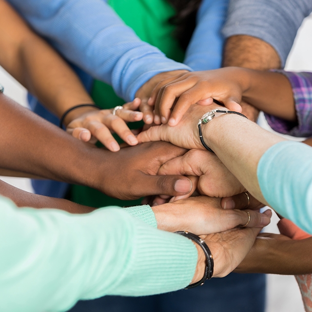 A diverse group of people standing in a circle, holding hands together in a show of unity and support.