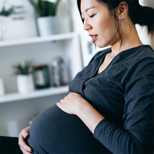 Young Asian woman sits and feels her pregnant stomach with both hands