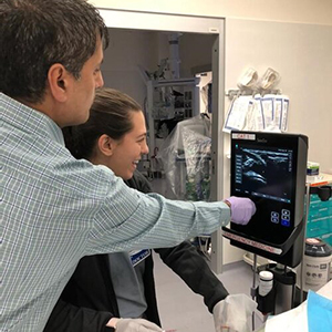 Student and doctor inspecting an ultrasound image while helping a patient