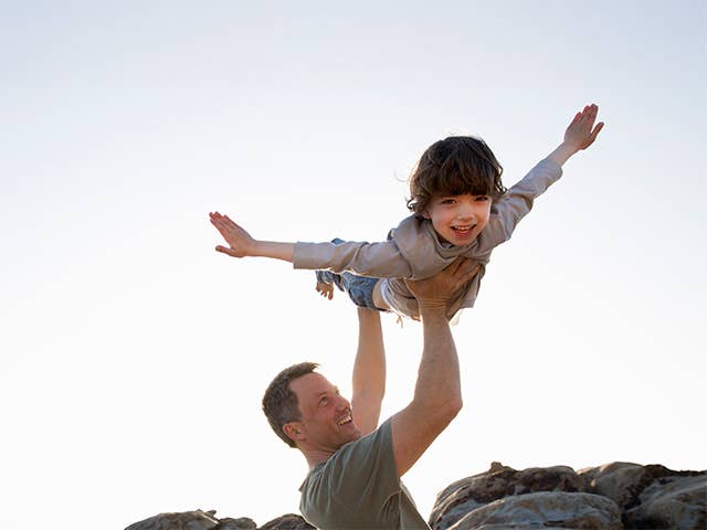 Middle aged man lifts his son into the air alongside the beach