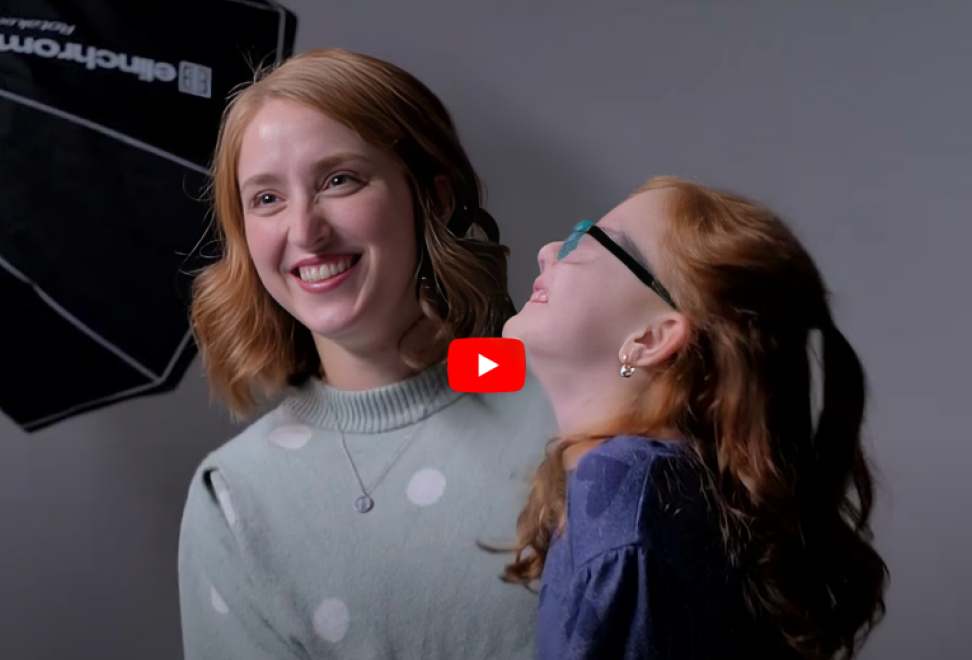 Two girls with red hair smiling and sitting in front of dark background