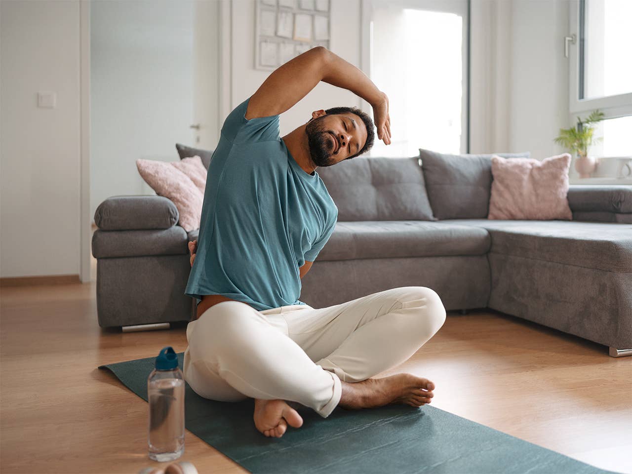 Young Black man sitting on a yoga mat in his living room and stretching his body to his left