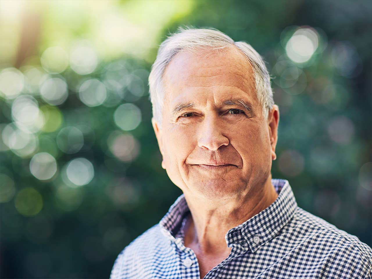 Elderly white man stands in the sunshine near trees