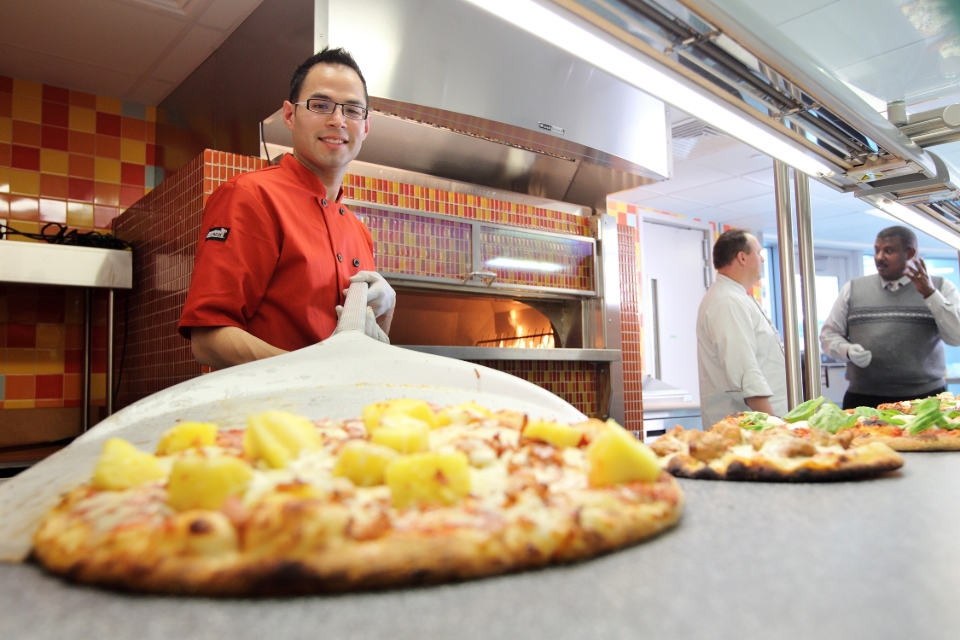 Male cook places freshly cooked pizza down to cool off